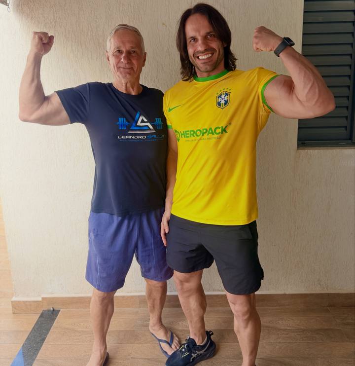 Leandro Salla ao lado do pai, os dois sorrindo e flexionando o braço